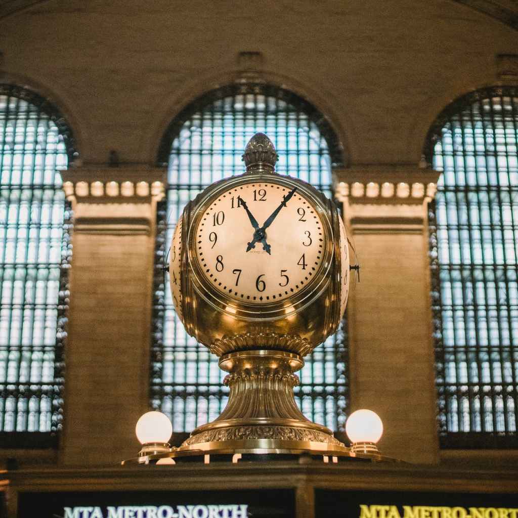 vintage golden clock in aged railway station terminal with arched windows